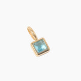 December birthstone charm, golden pendant with a blue gemstone on a white background