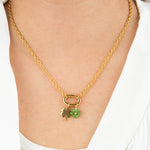 gold necklace with a clover and green flower charm on a person wearing a white shirt