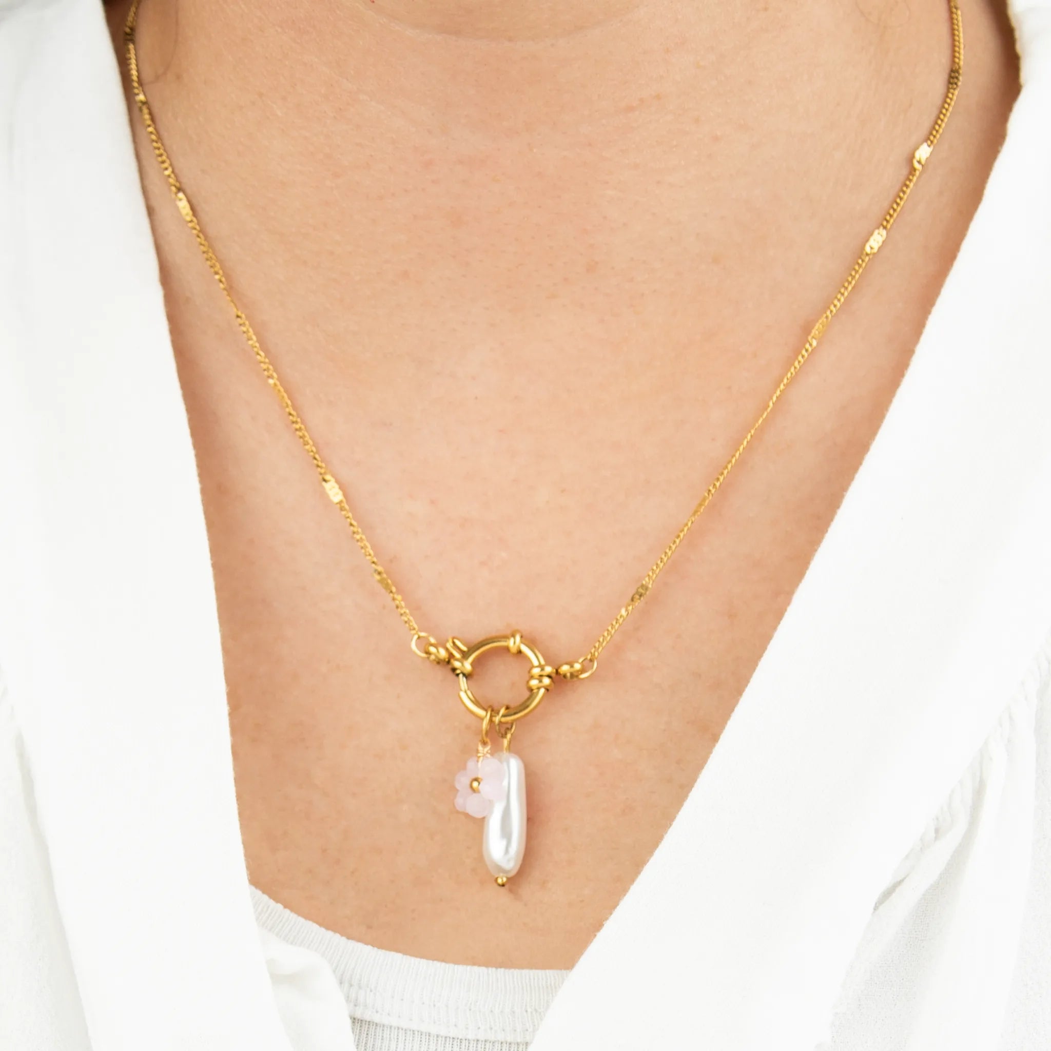 Gold necklace with a pearl and a fleur charm on a person wearing a white shirt