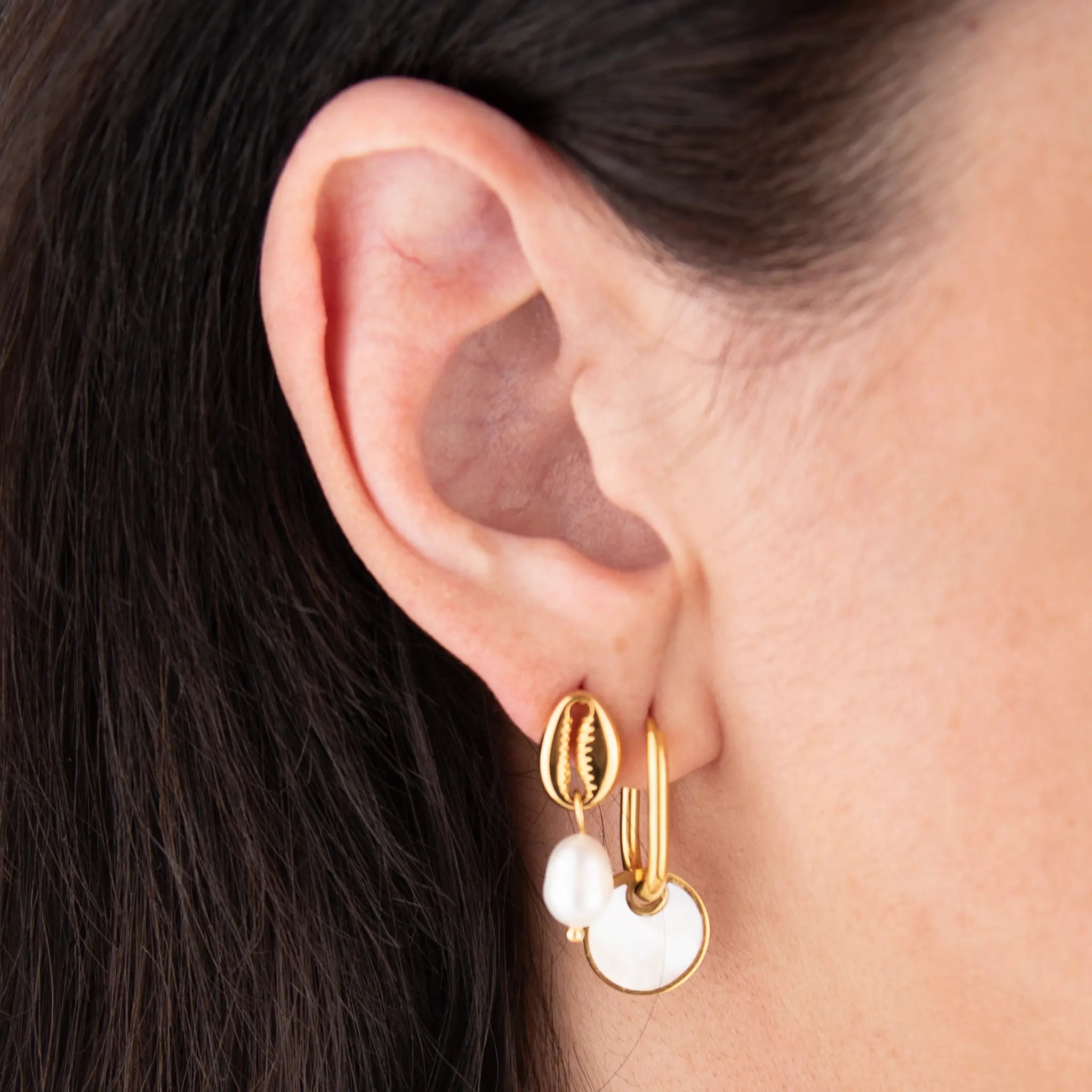 Close-up of an ear wearing golden and pearl earrings with dark hair.