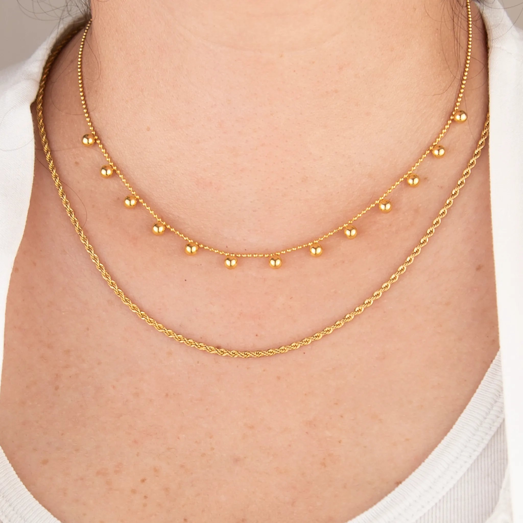 Golden drops set on a person's neck with a neutral background
