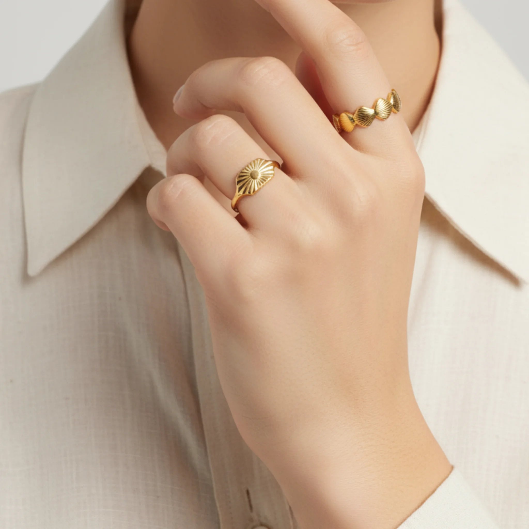 Hand wearing two gold rings with a white shirt background
