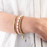 Three golden bracelets, one with white beads, on a person with a white shirt