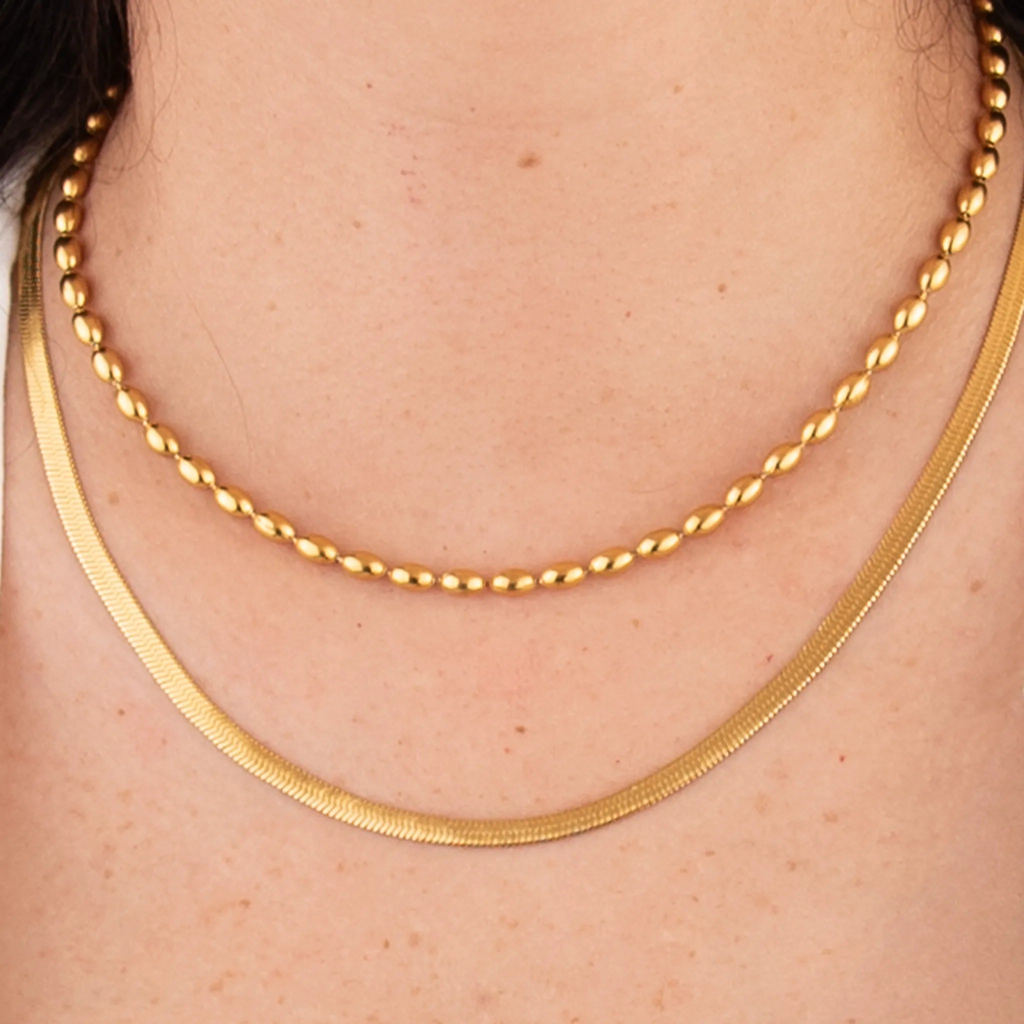 Two gold necklaces on a person's neck with a plain background