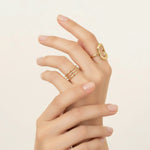 Hand wearing two gold rings on a beige background