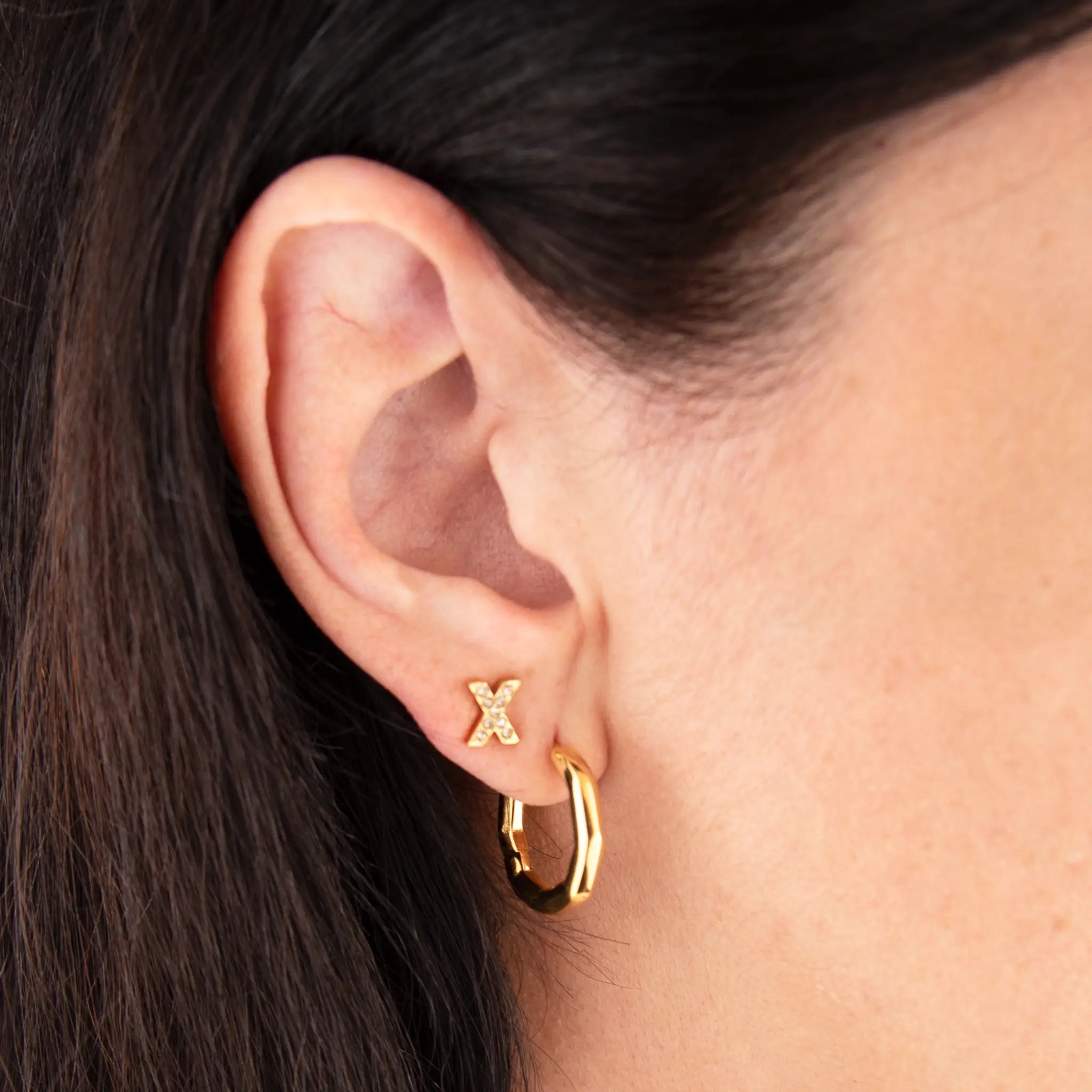 Golden xo duo hoops and studs worn by a person with dark hair.