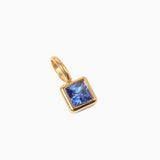 September birthstone charm, golden pendant with a blue gemstone on a white background