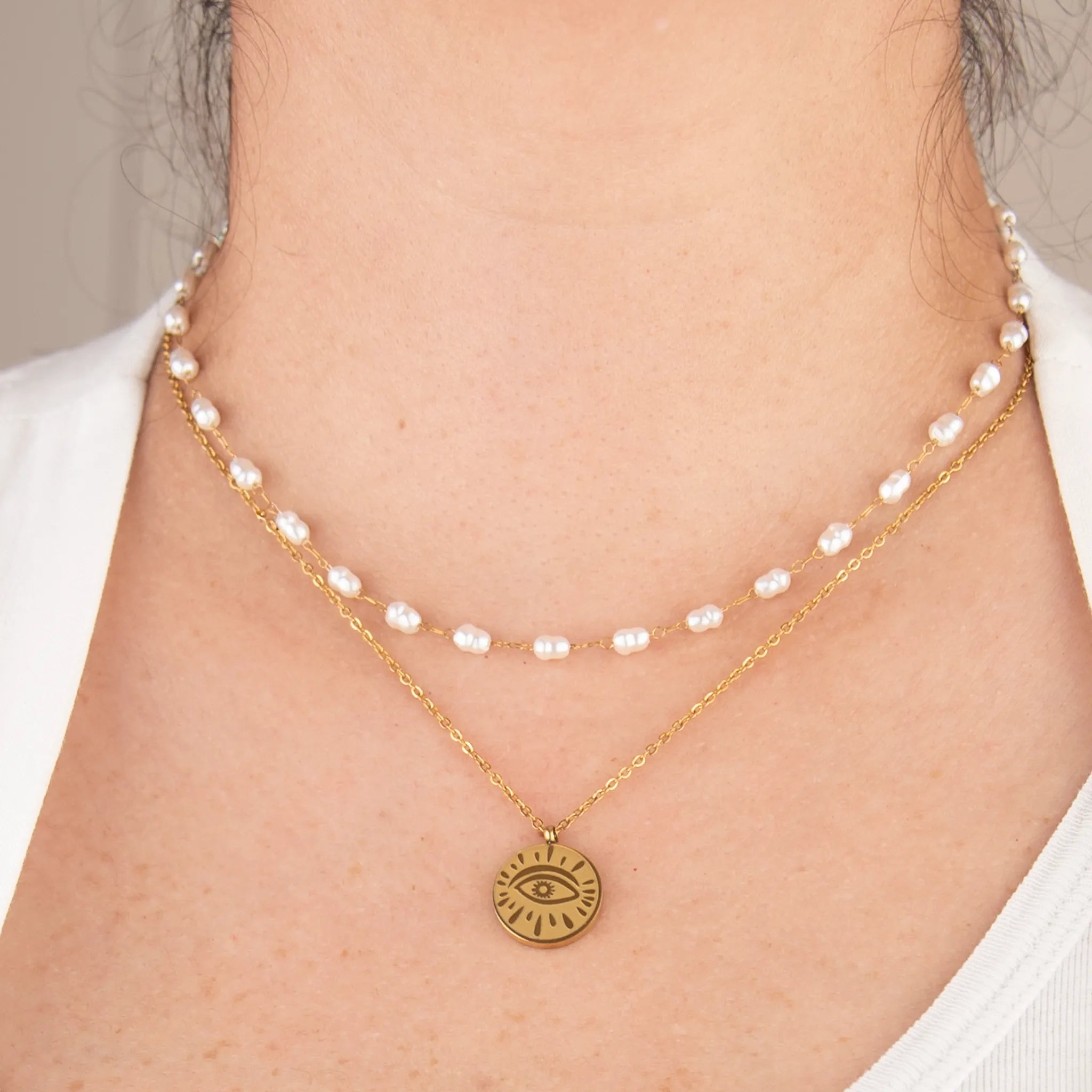 Two necklaces with pearls and a gold pendant on a person wearing a white top