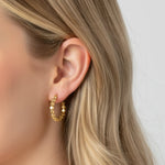 Close-up of a woman wearing gold beaded texture hoop earrings with a neutral background