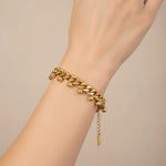 Gold chain bracelet with drops on a wrist against a beige background