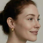 Close-up of a woman wearing gold hoop earrings with a neutral background