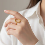 Gold bold oval ring on a finger against a neutral background