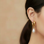 Gold hoop earring with a pearl drop worn by a person against a beige background