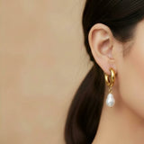 Gold hoop earring with a pearl drop worn by a person against a beige background