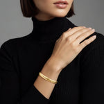 Woman wearing a gold braided cuff bracelet on a plain background