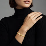 Woman wearing a gold braided cuff bracelet on a plain background