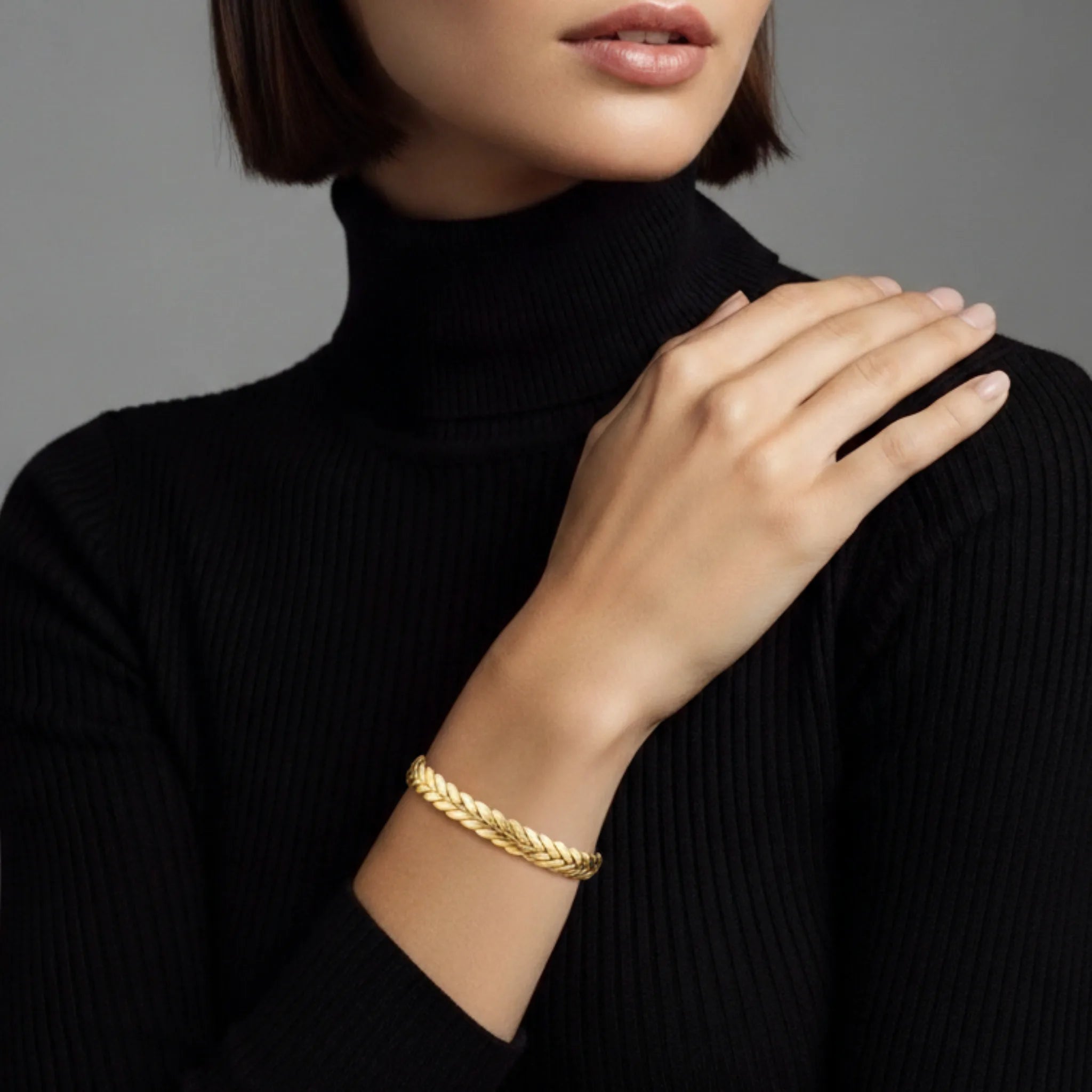 Woman wearing a gold braided cuff bracelet on a plain background