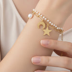 Gold bracelet with star and moon charm on a wrist against a neutral background