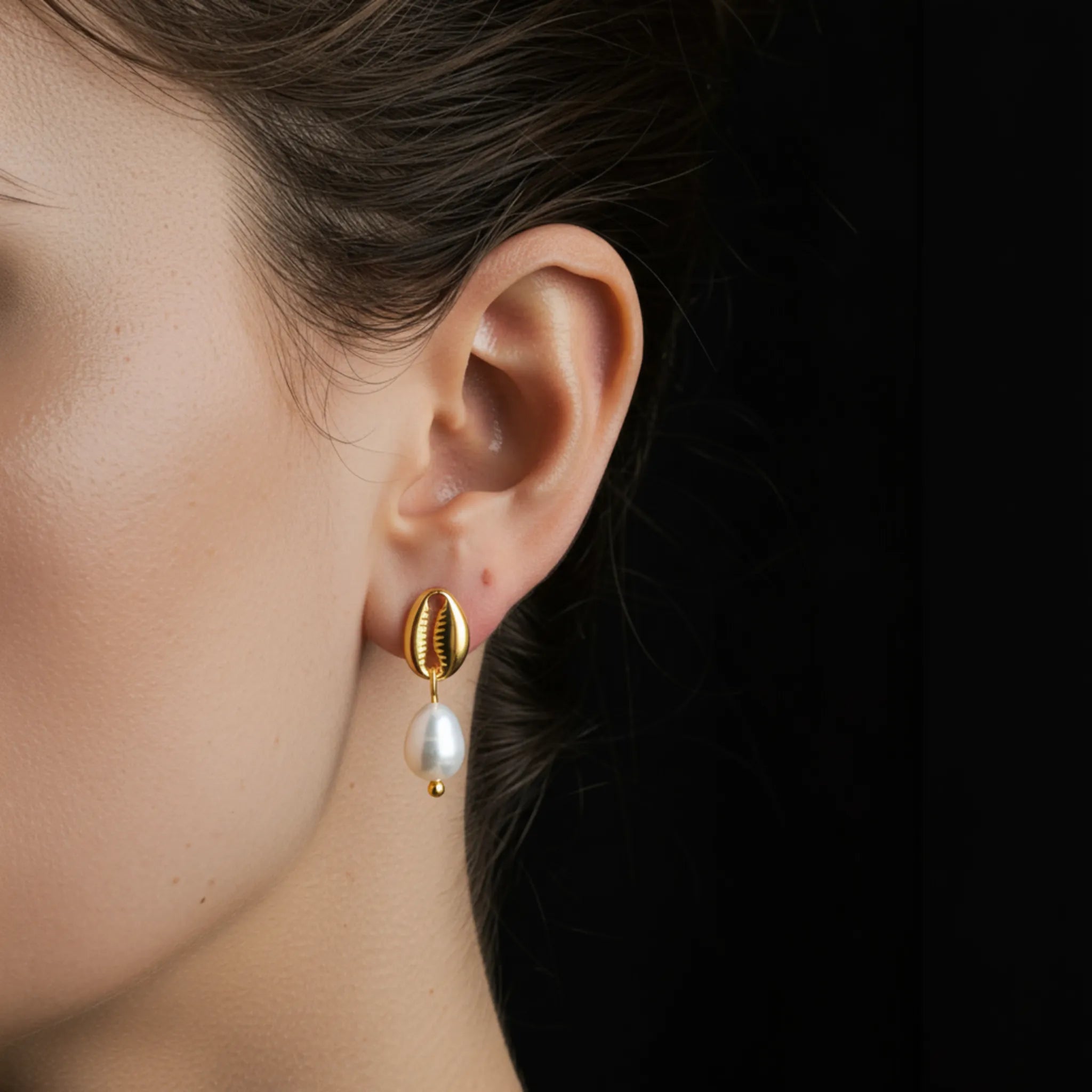 Gold earring with a pearl drop worn by a person against a dark background
