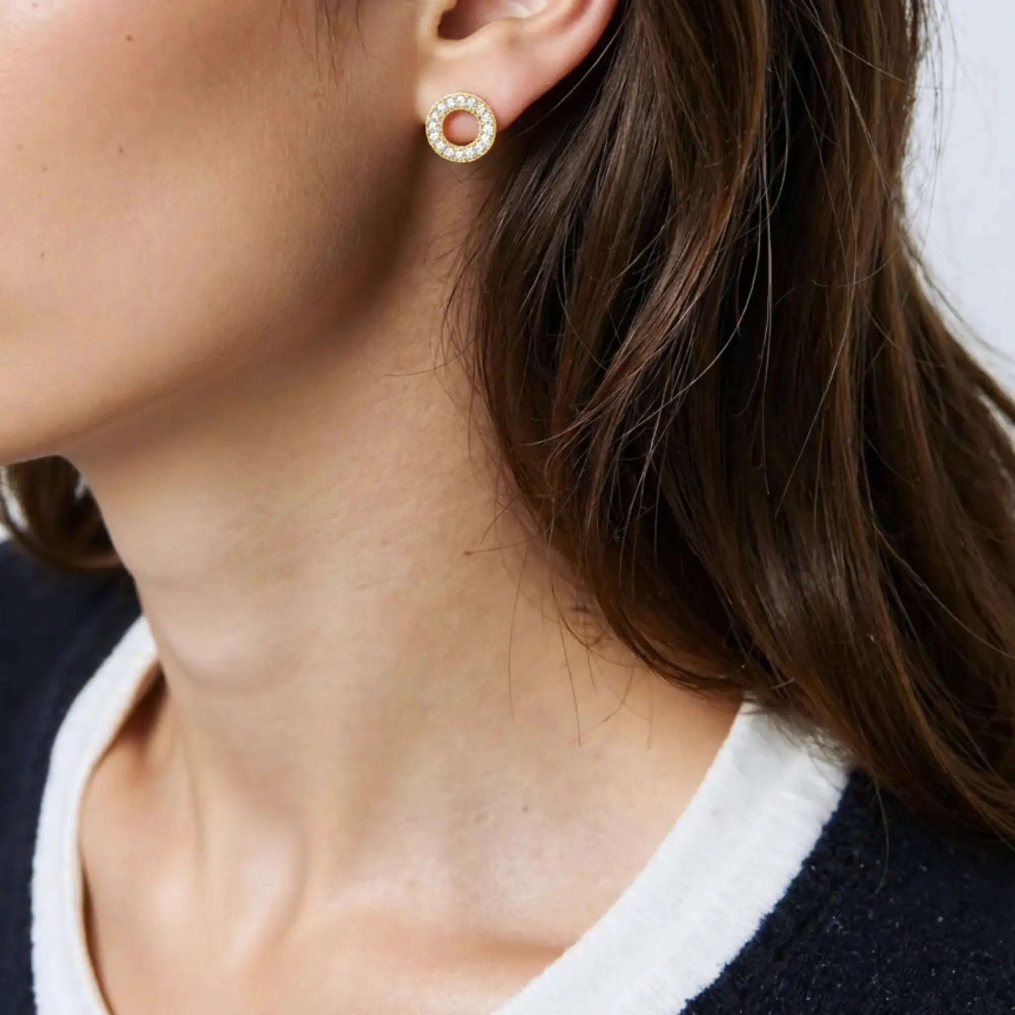 Close-up of a person wearing gold crystal circle studs earrings