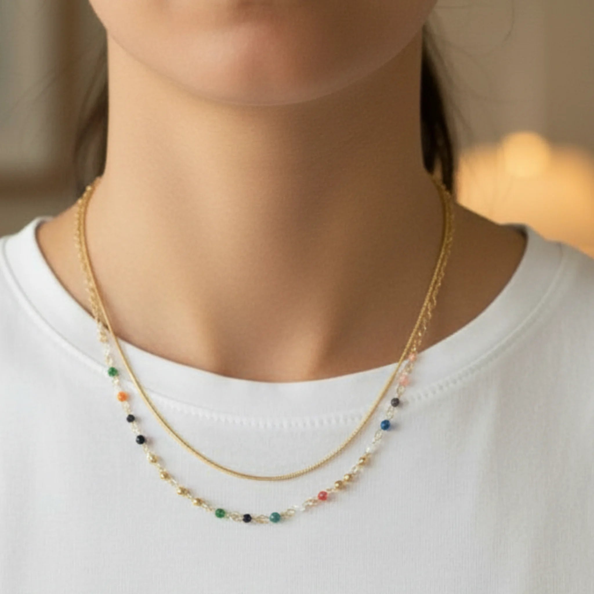 Gold double chain necklace with colorful beads worn by a person on a plain background