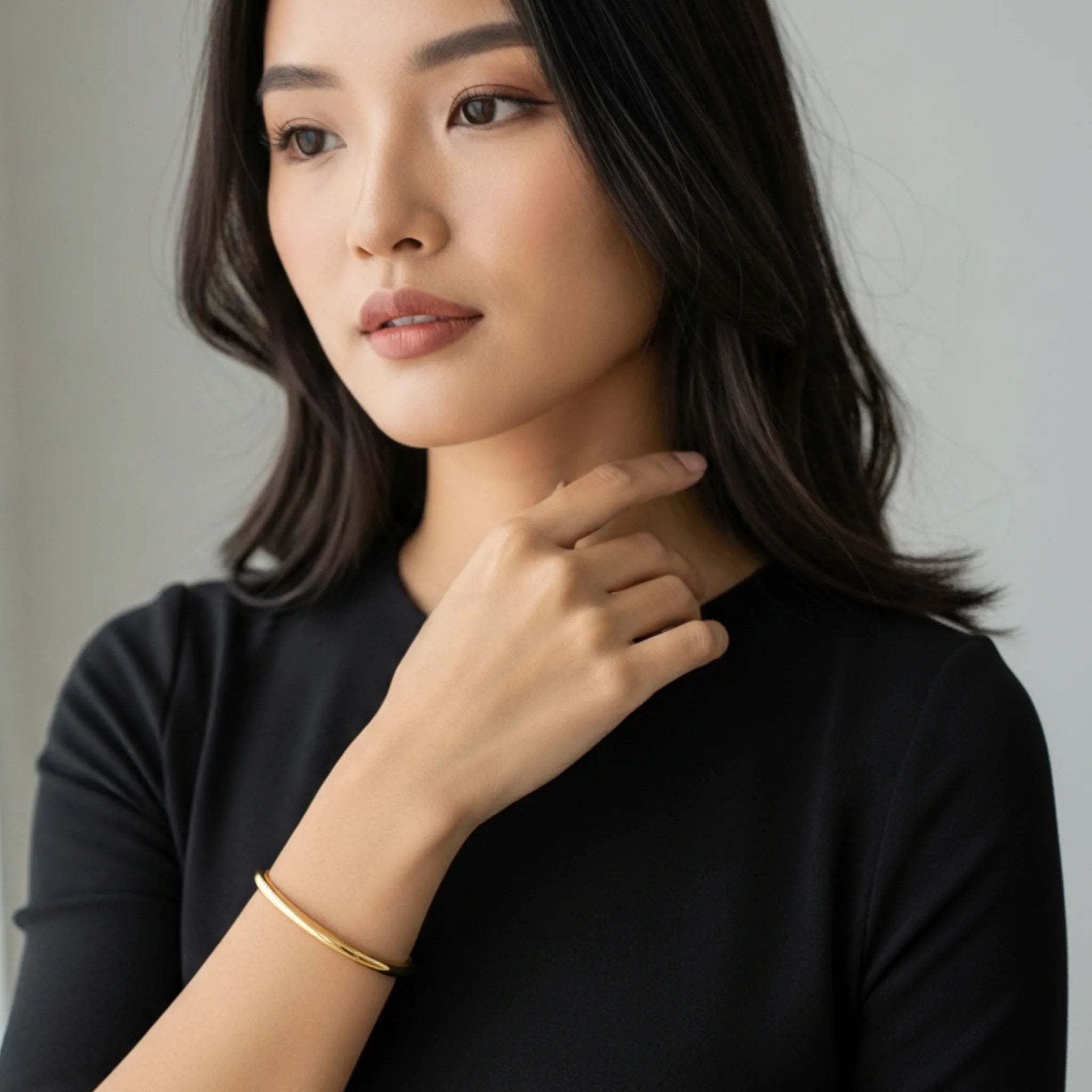 Woman wearing a black top with a gold essential cuff bracelet on a neutral background