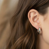 Close-up of an ear wearing a silver hoop earring with brown hair.