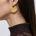 Gold geometric earring worn by a person with a neutral background