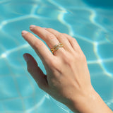 A hand wearing a gold cowrie shell ring in a swimming pool