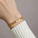 Gold disc chain bracelet on a wrist with a plain background