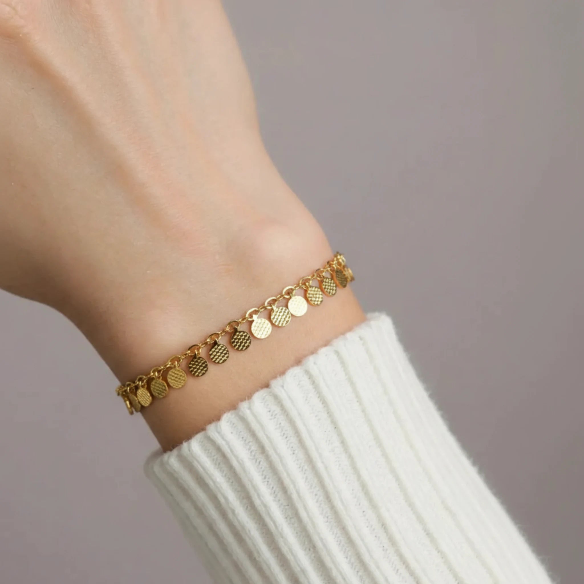 Gold disc chain bracelet on a wrist with a plain background