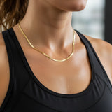 A woman wearing a gold herringbone chain necklace and a black top
