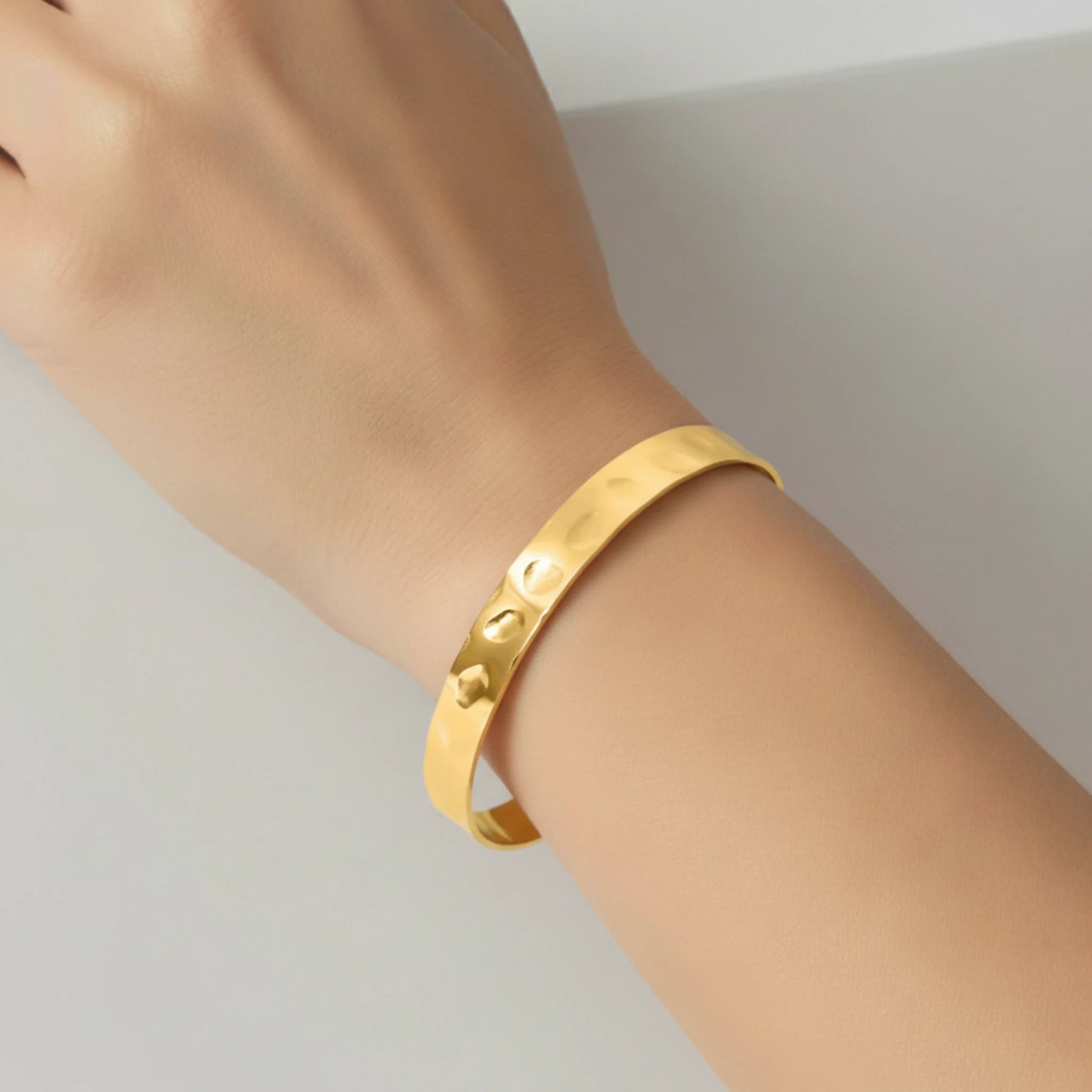 Gold bracelet on a wrist against a neutral background
