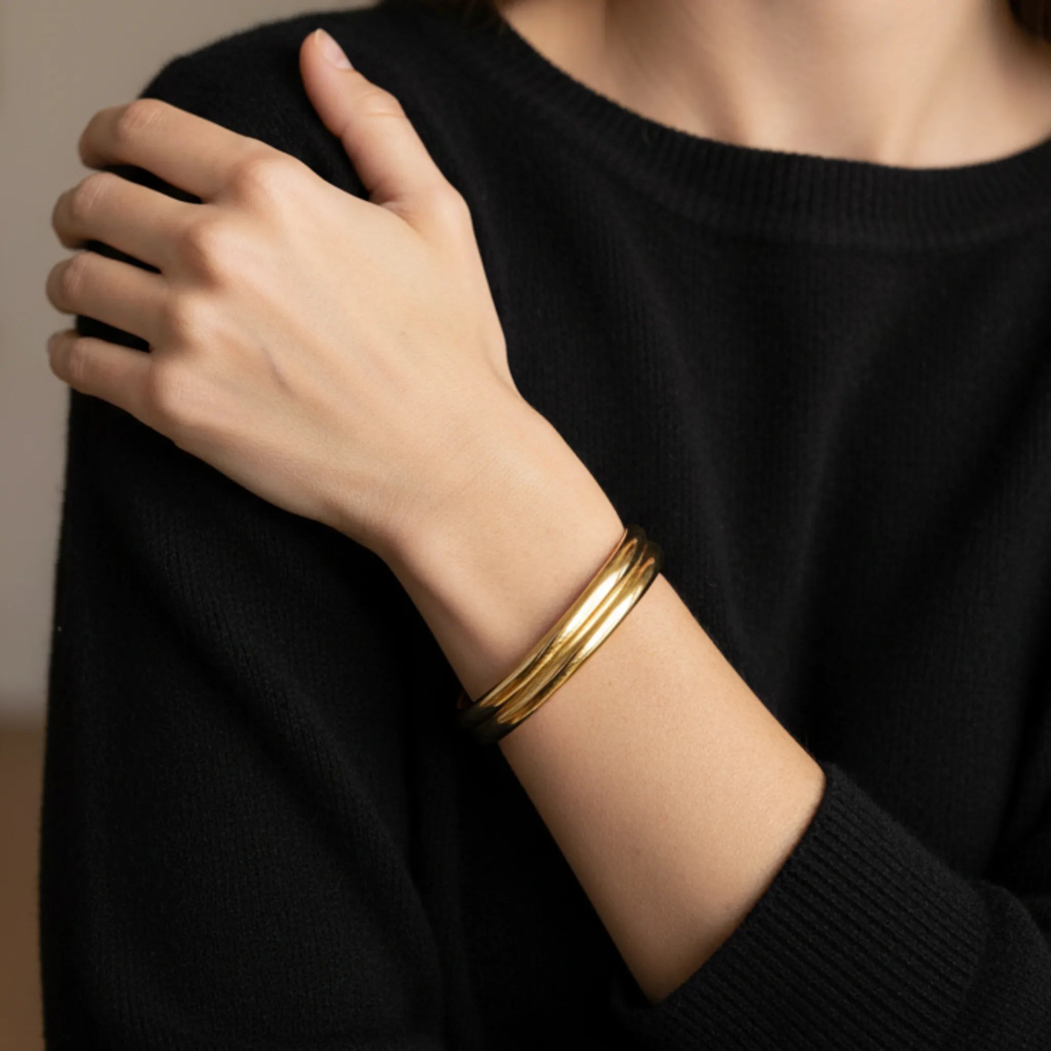 A woman wearing a minimalist gold cuff bracelet and a black shirt