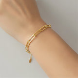 Gold chain bracelet on a wrist against a neutral background