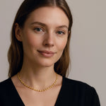 Woman wearing a gold oval bead choker necklace against a neutral background