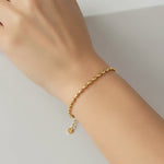 Gold oval bead bracelet on a wrist against a neutral background