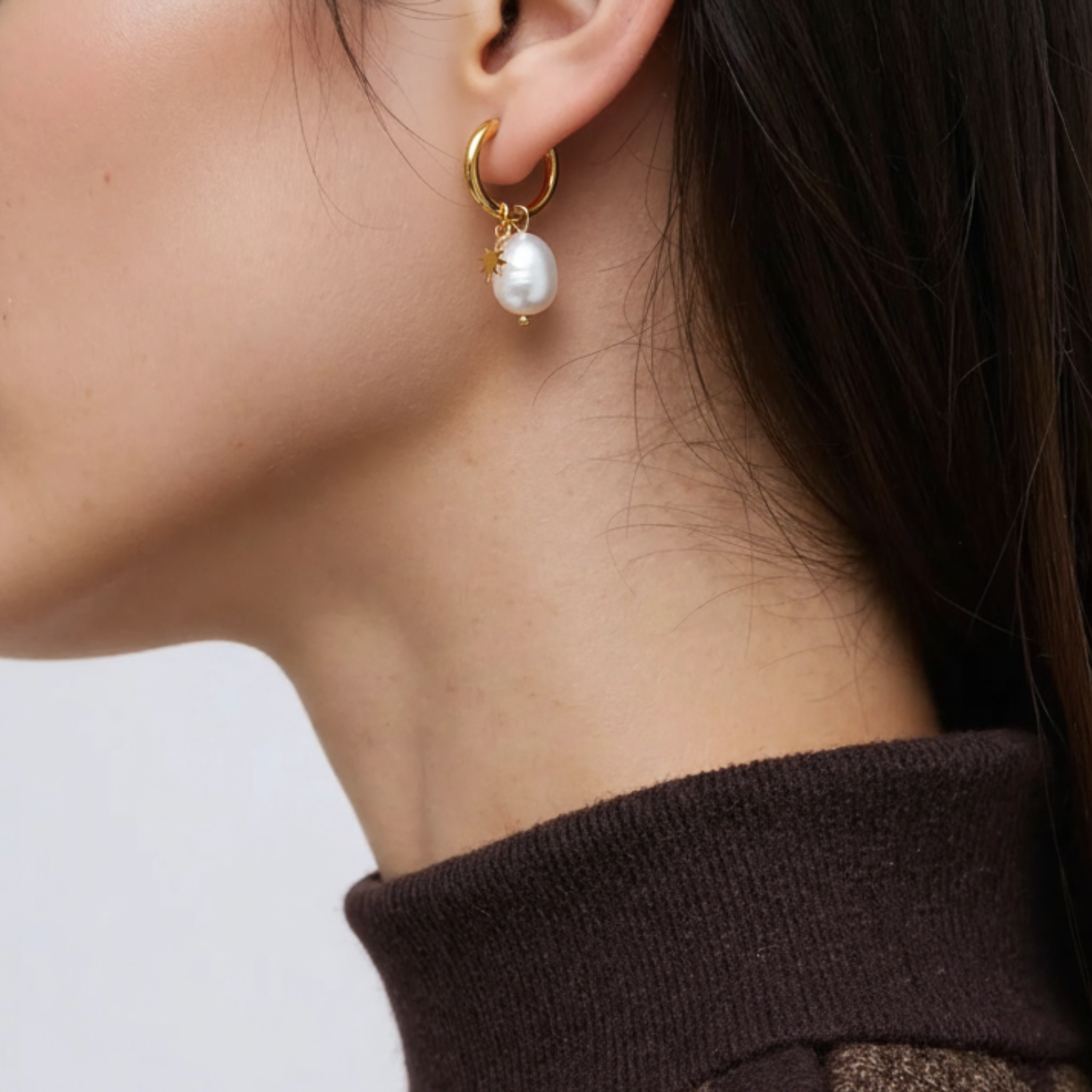 Pearl star hoop earring worn by a person on a plain background