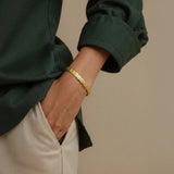 Woman wearing a gold shell pattern cuff bracelet on a beige background