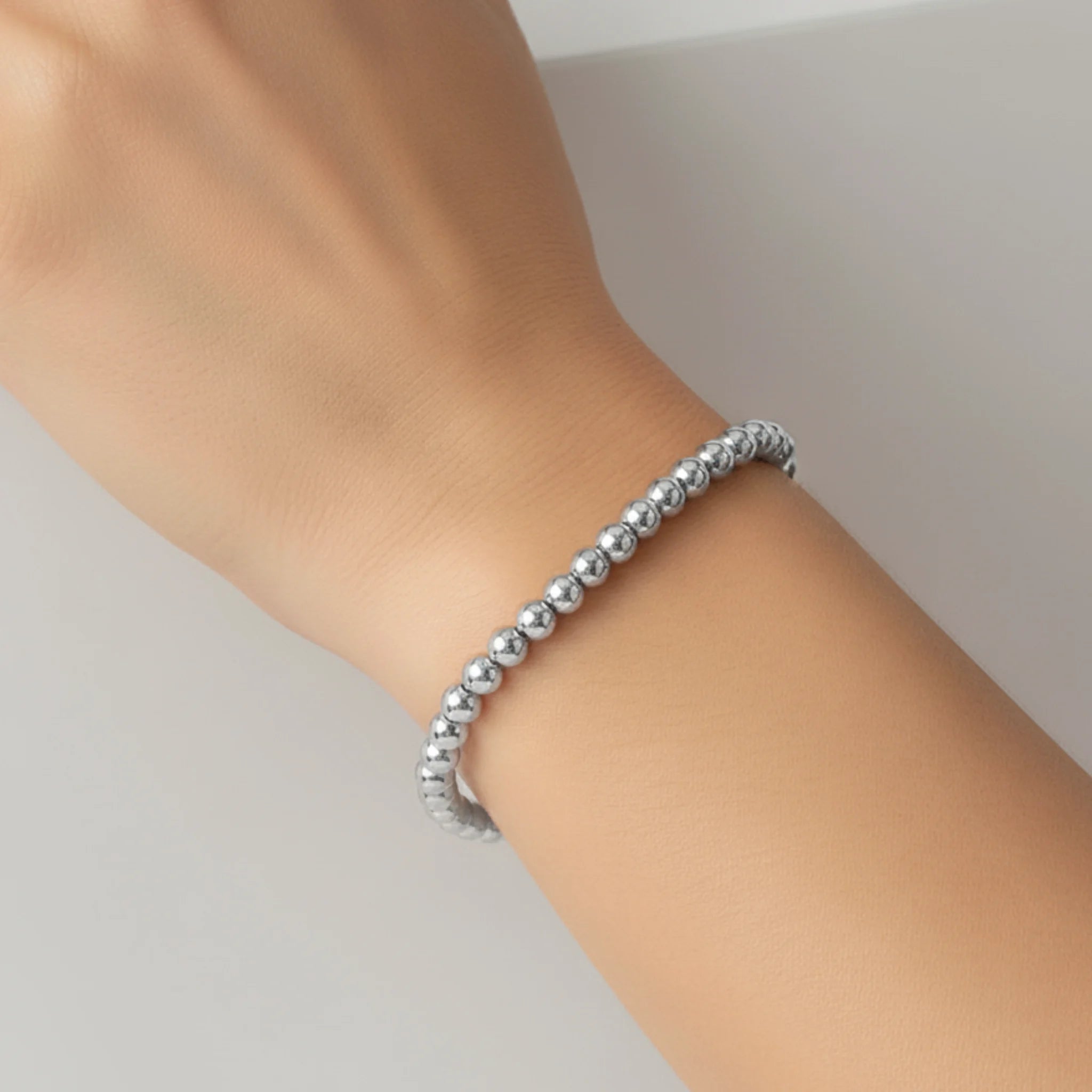 Silver beaded bracelet on a wrist against a neutral background