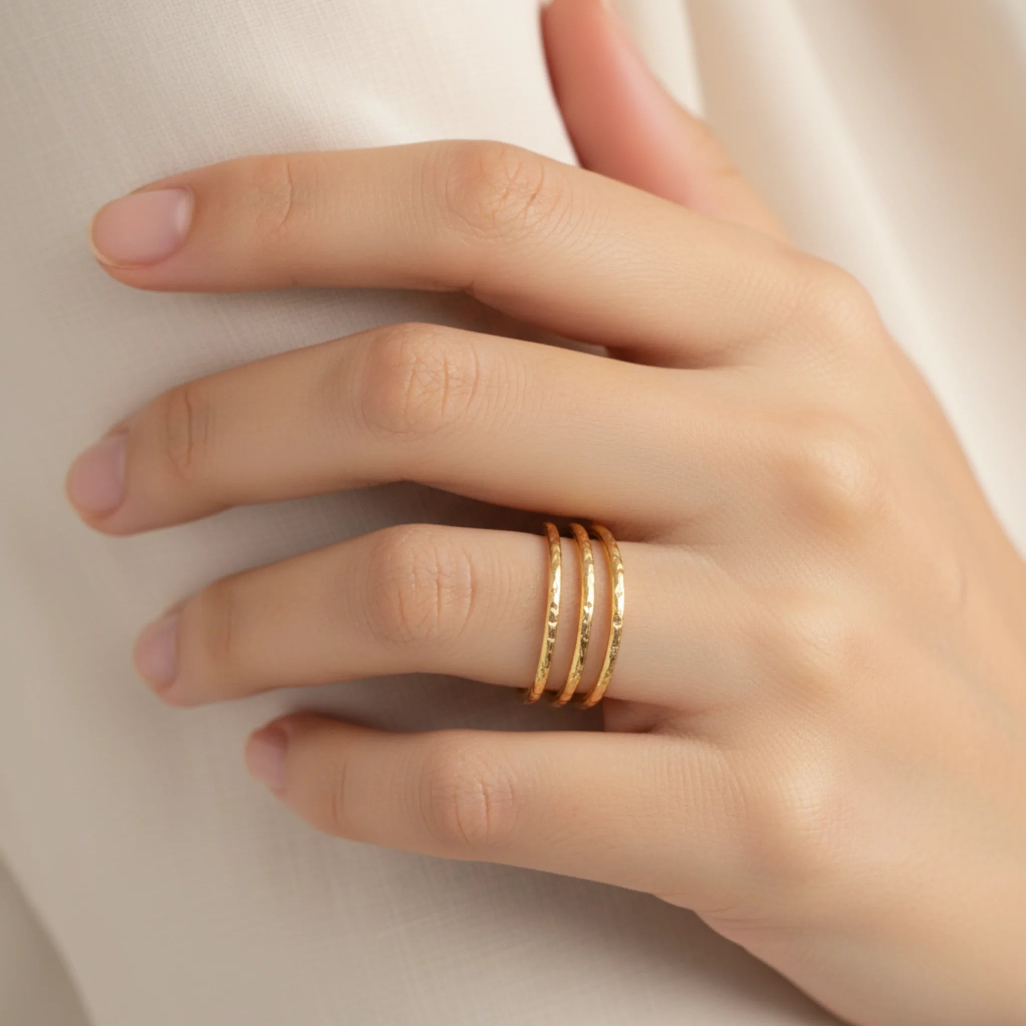 Hand wearing a textured triple band gold ring on a neutral background