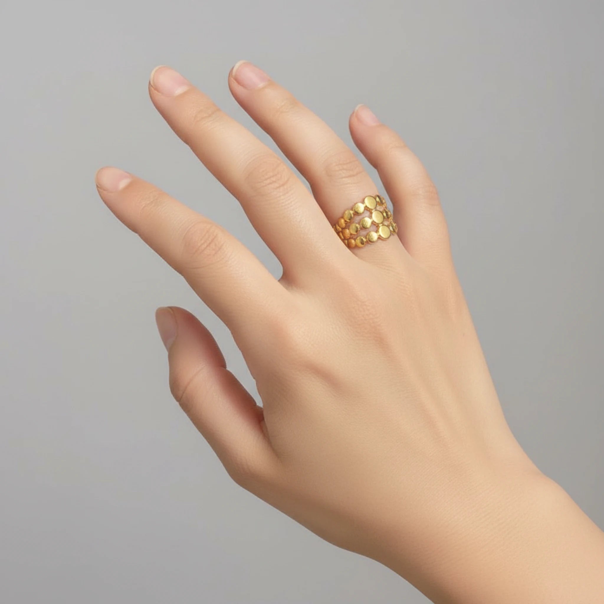Hand wearing a gold triple layer ring on a plain background