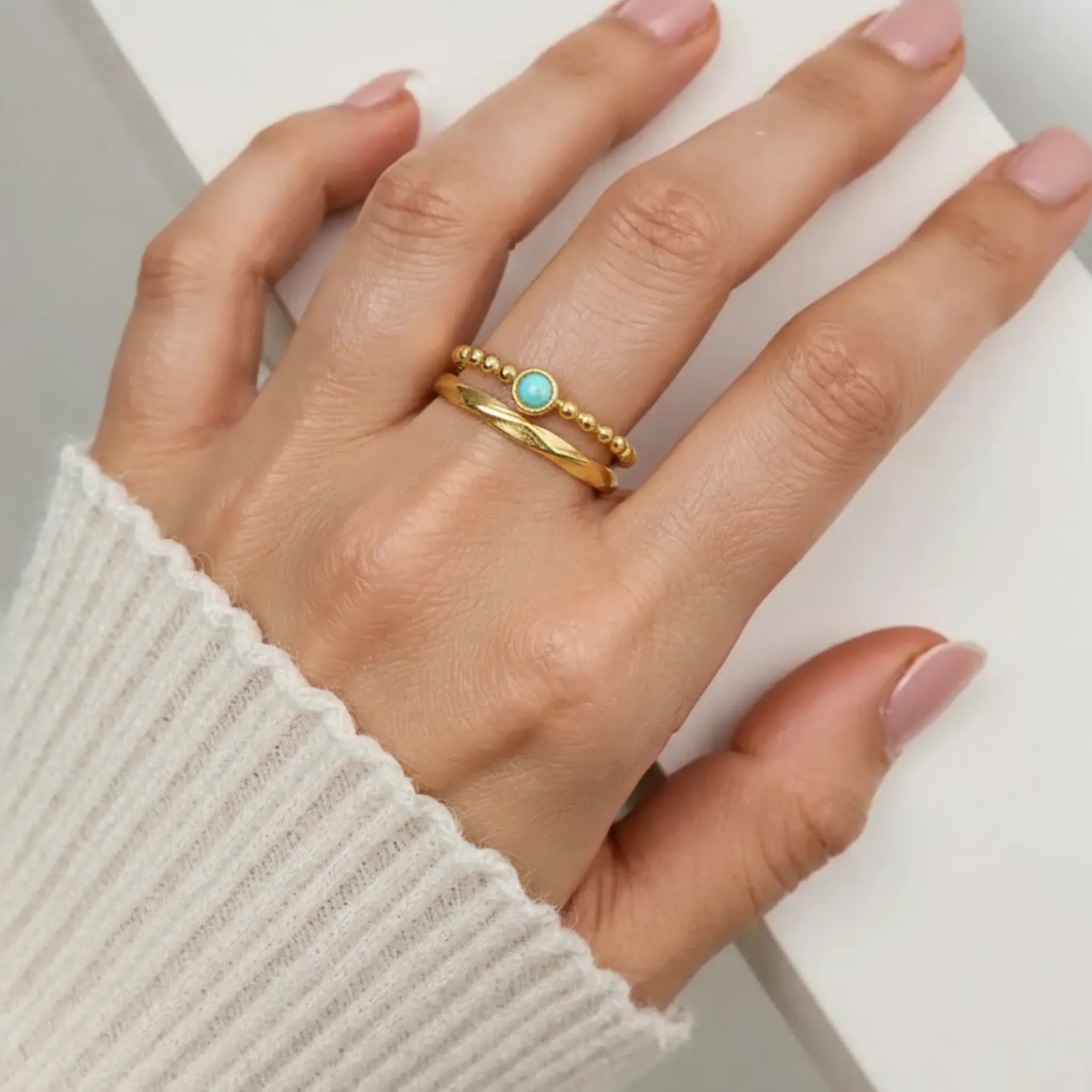 Hand wearing a gold ring with a turquoise stone on a white background