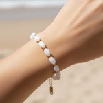 White shell beaded bracelet with a gold chain on a wrist against a neutral background